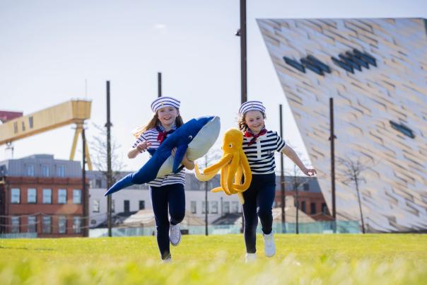 Two kids running across the grass outside Titanic Belfast as part of Belfast Maritime Festival Promotions.