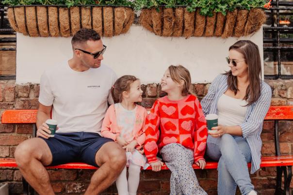 Family enjoying coffee and hot chocolate on a bench in Commercial Court Belfast