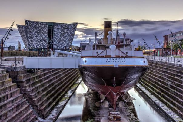 SS Nomadic with Titanic Belfast's building in the background at dusk.