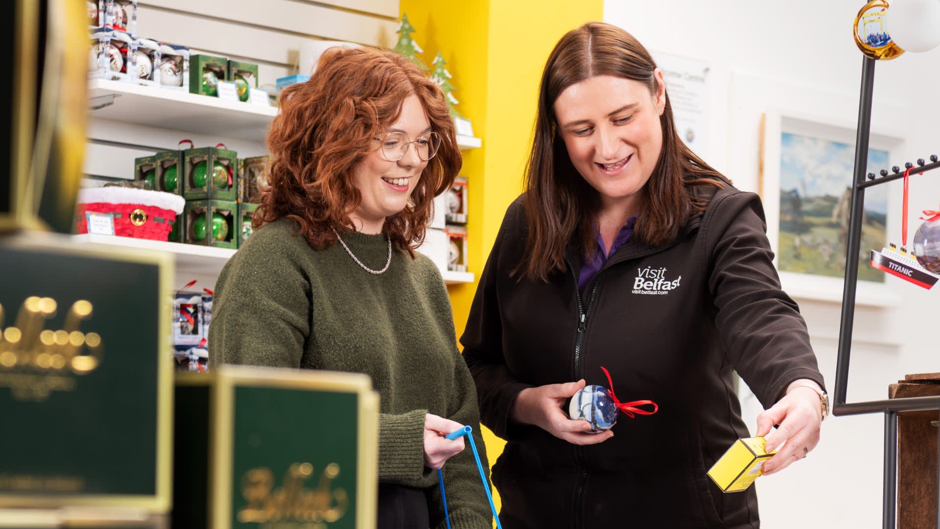 Shop assistant showing customer Christmas baubles in the Visit Belfast Welcome Centre