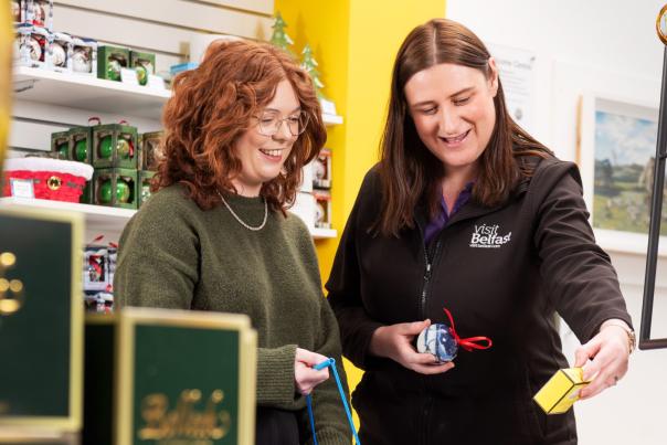 Shop assistant showing customer Christmas baubles in the Visit Belfast Welcome Centre